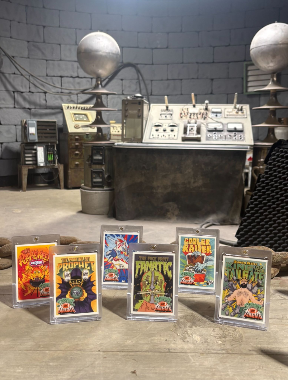 The image shows a collection of seven cards, each featuring a unique illustration and title, displayed on a concrete floor. The cards are arranged in a row, with the first card on the left featuring a fiery orange and red design, followed by a card with a blue and white design, and so on. The cards are encased in clear